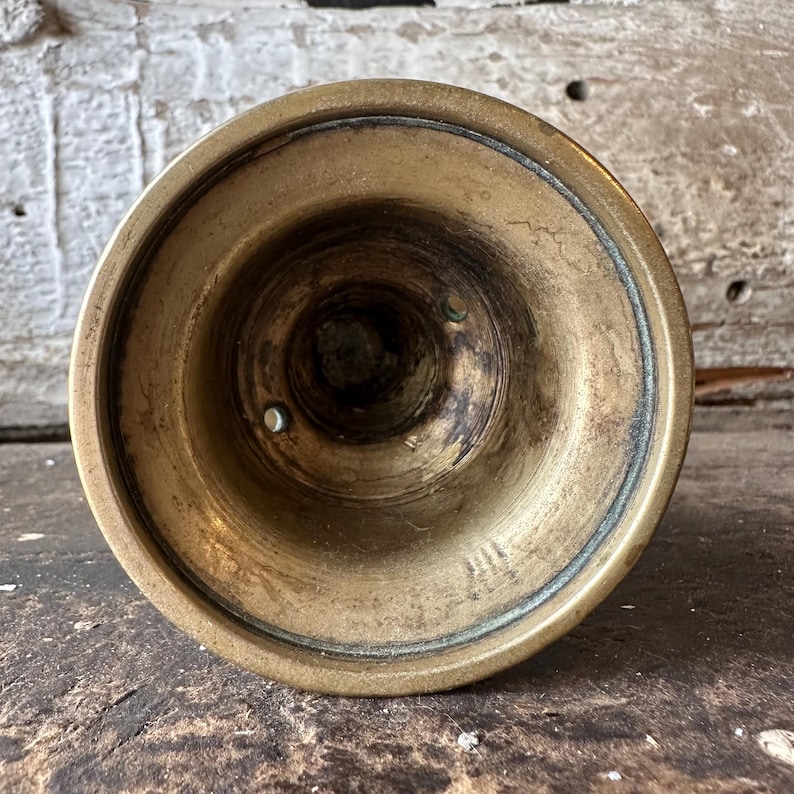 May include: A close-up view of the bottom of a brass candlestick holder. The interior is dark with signs of age and use. The exterior has a golden hue with a darker ring around the rim. The candlestick holder is likely vintage.