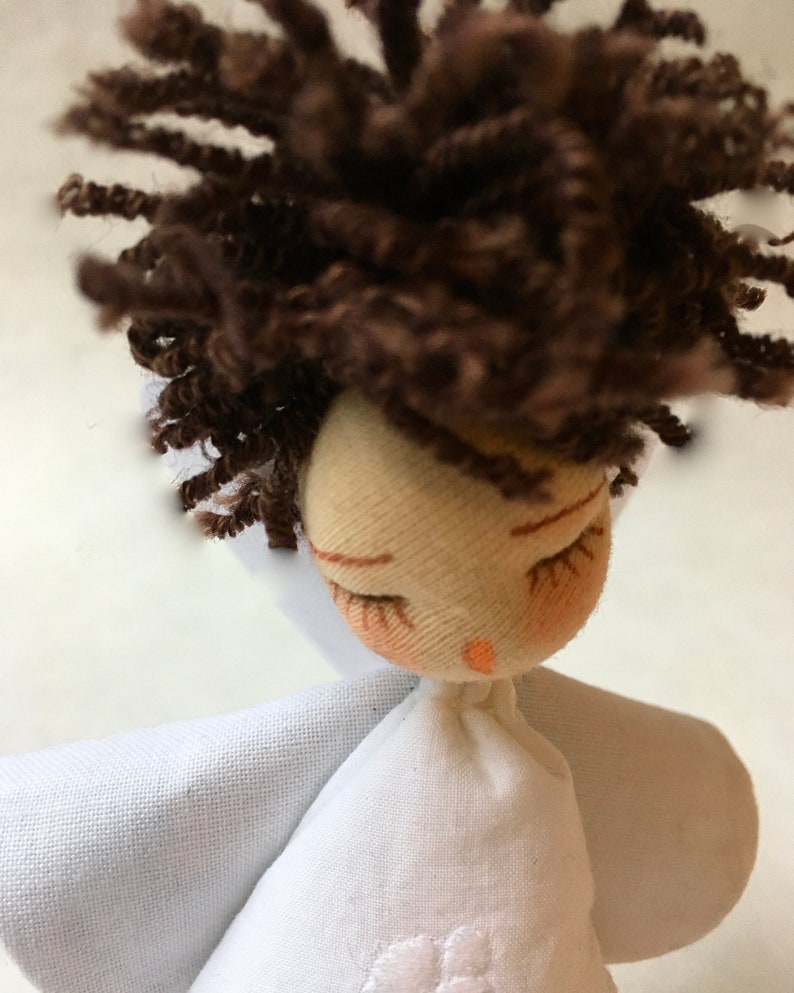 May include: A handmade doll with brown curly hair, closed eyes, and a white dress with a flower embroidered on the front.