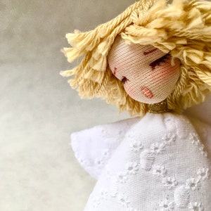 May include: A handmade doll with blonde yarn hair, a white dress with embroidered details, and a gold-colored halo.