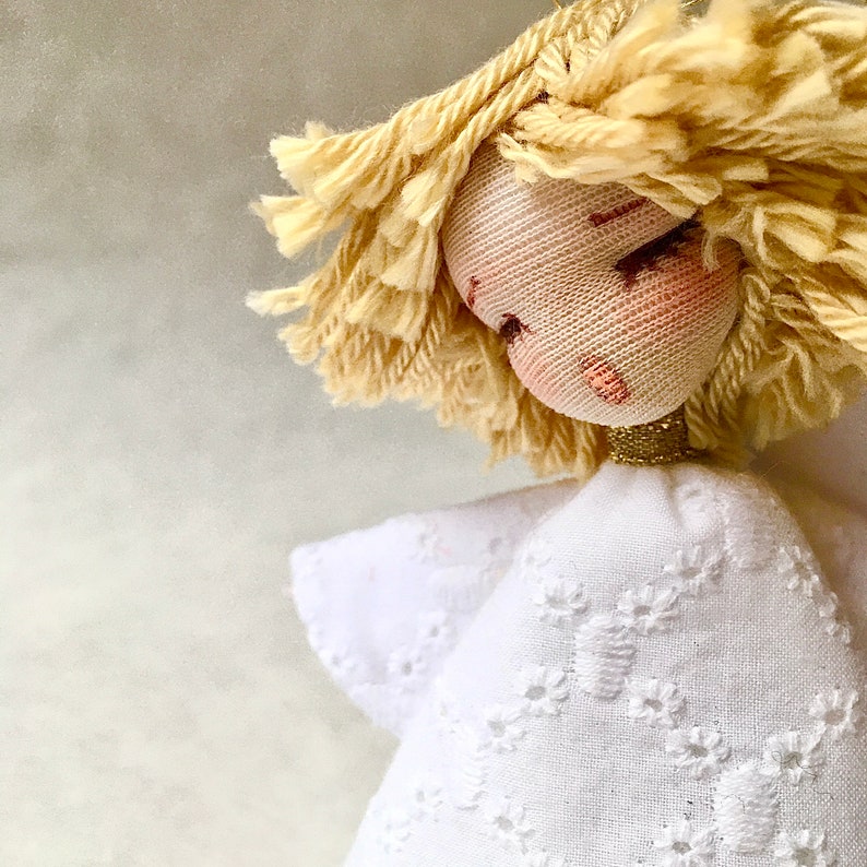 May include: A handmade doll with blonde yarn hair, a white dress with embroidered details, and a gold-colored halo.