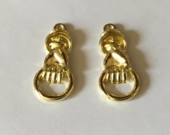 May include: Two gold-colored metal charms in the shape of a hand holding a ring. The charms are detailed and have a vintage look.