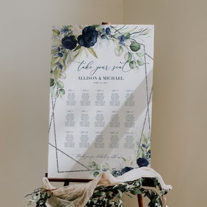 May include: A wedding seating chart with a watercolor design featuring blue flowers and green leaves. The chart is titled "Take your seat" and lists the names of guests assigned to each table. The text "Allison & Michael" and "April 16, 2023" is also included.