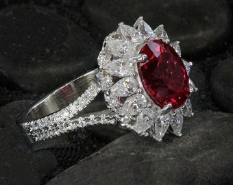 May include: A silver ring with a large red gemstone surrounded by smaller white gemstones.