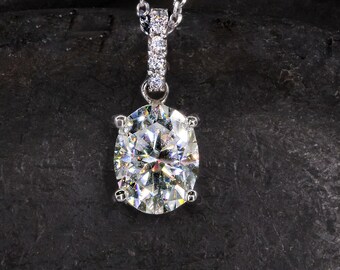 May include: A silver chain necklace with a large oval-shaped diamond pendant. The diamond is set in a silver bezel and has a bright, clear sparkle.