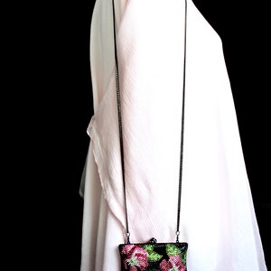 May include: A small black evening bag with a chain strap. The bag is decorated with pink and green floral embroidery.