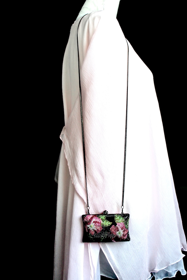 May include: A small black evening bag with a chain strap. The bag is decorated with pink and green floral embroidery.
