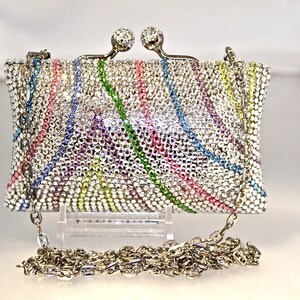 May include: A silver clutch purse covered in iridescent rhinestones with a rainbow pattern. The purse has a chain strap.