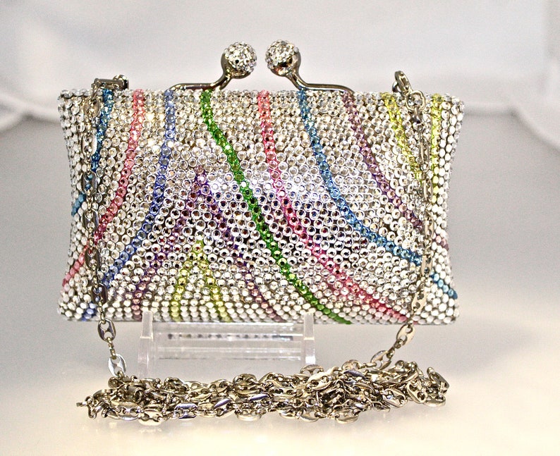 May include: A silver clutch purse covered in iridescent rhinestones with a rainbow pattern. The purse has a chain strap.