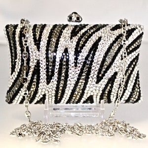 May include: A black and white zebra print clutch purse with a silver chain strap. The purse is covered in rhinestones.
