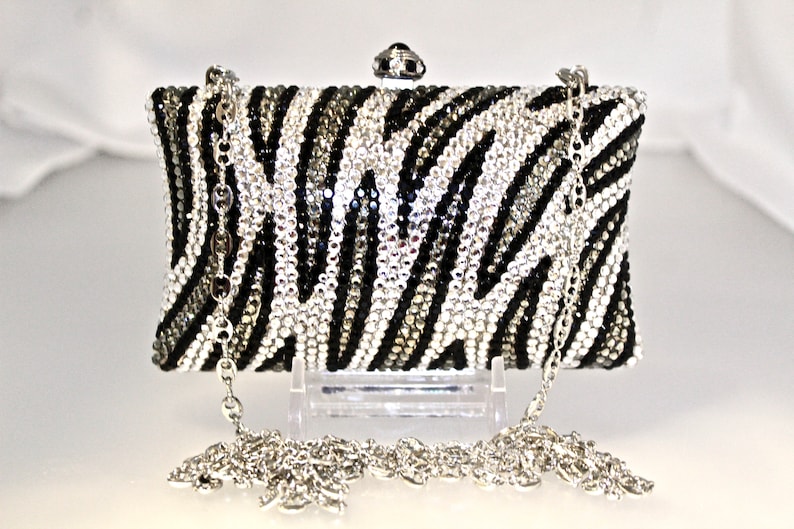 May include: A black and white zebra print clutch purse with a silver chain strap. The purse is covered in rhinestones.