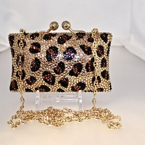 May include: A small gold chain purse with a leopard print design. The purse is covered in rhinestones and has a gold clasp.
