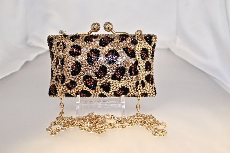 May include: A small gold chain purse with a leopard print design. The purse is covered in rhinestones and has a gold clasp.