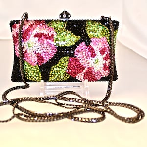 May include: A black evening bag with a chain strap. The bag is covered in rhinestones and features a floral design with pink, green, and clear rhinestones.