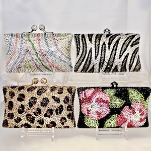 May include: Four different rhinestone clutch purses. The purses are all the same size and shape, but they have different patterns. One purse has a zebra print, one has a leopard print, one has a floral print, and one has a swirl pattern.