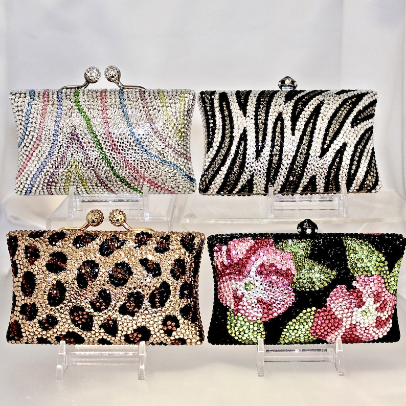 May include: Four different rhinestone clutch purses. The purses are all the same size and shape, but they have different patterns. One purse has a zebra print, one has a leopard print, one has a floral print, and one has a swirl pattern.