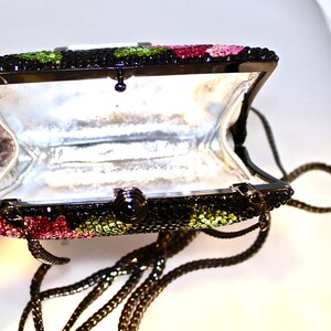 May include: A black evening bag with a chain strap. The bag is covered in rhinestones and has a floral design with pink, green, and black accents.