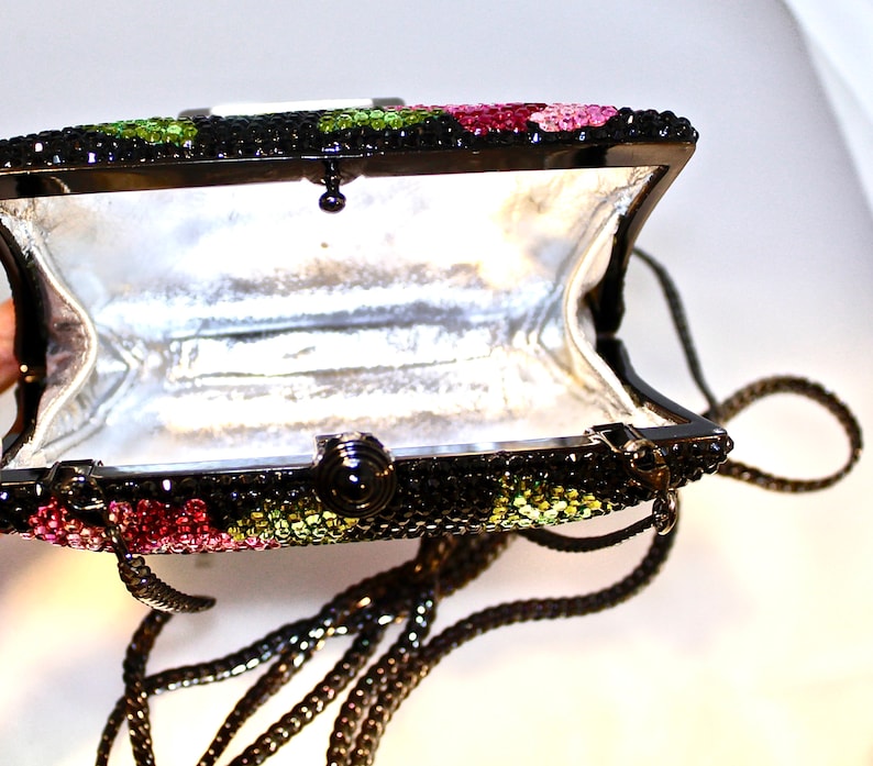 May include: A black evening bag with a chain strap. The bag is covered in rhinestones and has a floral design with pink, green, and black accents.