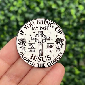May include: A white and black round pin with the text "If you bring up my past, you should know that Jesus dropped the charges." The pin features a cross, roses, and stars.