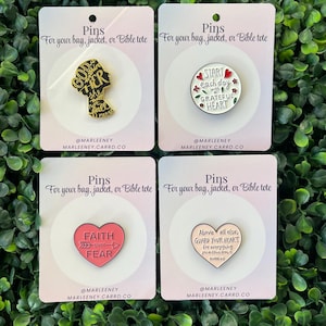 May include: Four enamel pins on cards, each with a different design and message. One pin features a silhouette with text, another says "Start each day with a grateful heart." The others say "Faith over Fear" and "Guard your heart."