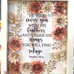 May include: White framed artwork with a clear front, featuring paper flowers in shades of peach and cream, gold glitter accents, and two gold butterflies. The artwork includes the text "HE WILL cover you with his feathers and under his wings you will find refuge Psalms 91:4."
