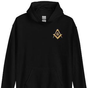 Könnte beinhalten: Schwarzer Kapuzenpullover mit einem goldenen Freimaurer-Symbol auf der Vorderseite. Das Symbol ist ein Quadrat und ein Zirkel mit einem 'G' in der Mitte.