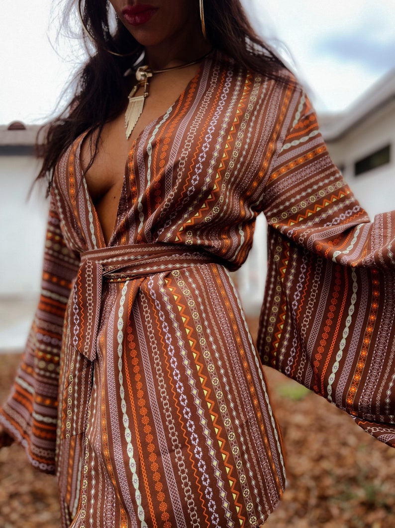 Puede incluir: Un vestido de envoltura marr&oacute;n y naranja con estampado geom&eacute;trico, cuello en V profundo y mangas largas. El vestido tiene un cintur&oacute;n de lazo en la cintura.