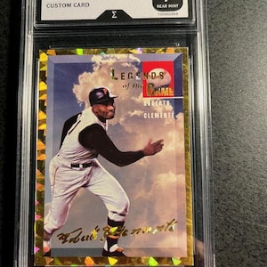 K&ouml;nnte beinhalten: Eine Roberto Clemente Legends of the Game Custom Card, bewertet mit Near Mint 7. Die Karte zeigt ein Farbbild von Clemente in Baseball-Uniform vor einem bew&ouml;lkten Himmel. Die Karte ist in einem Schutzhalter eingeschlossen.