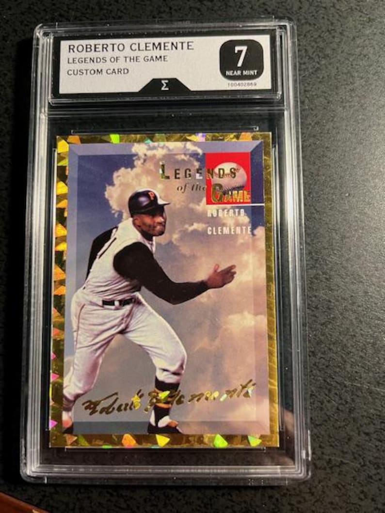 K&ouml;nnte beinhalten: Eine Roberto Clemente Legends of the Game Custom Card, bewertet mit Near Mint 7. Die Karte zeigt ein Farbbild von Clemente in Baseball-Uniform vor einem bew&ouml;lkten Himmel. Die Karte ist in einem Schutzhalter eingeschlossen.