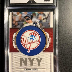 May include: A 2023 Topps Aaron Judge trading card encased in a protective plastic slab with an 8 Mint grade. The card features a photograph of Aaron Judge batting, a circular New York Yankees logo patch, and the text NYY printed on a white background.