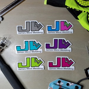 May include: Six different color variations of a logo sticker with the text "James West Welding" and the initials "JW" in a stylized font. The logo is a black outline of a "J" and a "W" with a stylized arrow pointing up and to the right.