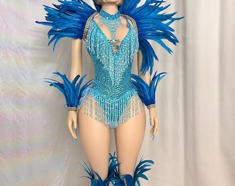 May include: A turquoise blue, beaded bodysuit with matching feather accents. The costume features a plunging neckline, fringe detailing, and is adorned with blue feathers on the shoulders, wrists, and ankles. The mannequin is wearing a wig.