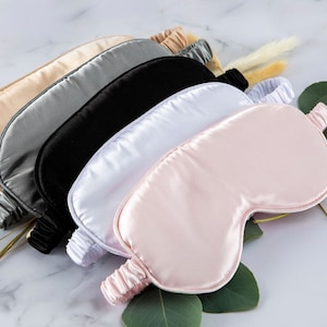 May include: Six silk sleep masks in different colours: beige, grey, black, white, and pink. The masks are arranged in a stack, with the pink mask on top.