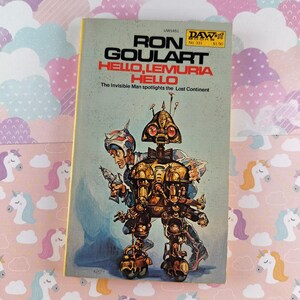 以下が含まれることがあります： ロン・ゴーラート著「HELLO, LEMURIA, HELLO」というタイトルのヴィンテージペーパーバック。表紙には、ロボットと光線銃を持った男のレトロなSFイラストが描かれています。本は黄色の背表紙で、ピンク色の背景に置かれています。