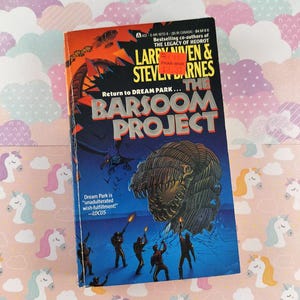 May include: A paperback book titled "The Barsoom Project" by Larry Niven and Steven Barnes. The cover features a large, monstrous creature and figures with weapons. The background is a mix of orange, blue, and black.