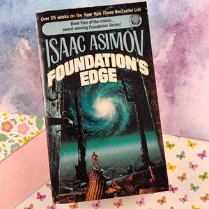 Puede incluir: Una portada de libro de bolsillo con fondo negro y texto blanco. El título es "Foundation's Edge" de Isaac Asimov. La portada presenta una escena futurista con una figura de pie sobre una estructura en ruinas sobre un fondo de galaxia giratoria.