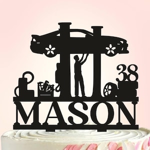 Puede incluir: Topper de pastel en silueta negra de un coche en un elevador con un mecánico trabajando en él. El topper también incluye el nombre "MASON" y el número "38".