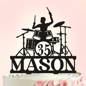 May include: Black silhouette of a drummer playing a drum set with the number 35 and the name Mason below. The cake topper is made of acrylic and is perfect for a birthday cake.