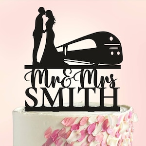 May include: Black silhouette cake topper featuring a bride and groom kissing in front of a train with the text "Mr. & Mrs. SMITH" underneath.