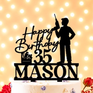 Op de afbeelding: Een zwarte taarttopper met de tekst Happy Birthday, het getal 35 en de naam MASON. Het ontwerp bevat een silhouet van een persoon die een boormachine vasthoudt en een kleine gereedschapskist gevuld met diverse handgereedschappen op een voet.