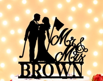 Op de afbeelding: Een zwarte taarttopper in silhouetvorm met een koppel, waarbij één persoon een golfclub vasthoudt en de ander bij een golfvlag staat. De tekst "Mr & Mrs" staat in schrijfletters boven de naam "BROWN" in blokletters.