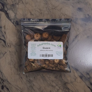 May include: A clear plastic bag filled with dried brown Guaico (Mikania Micrantha) herb pieces. The bag has a label that reads "AlkaHerbs.com" and "Guaco (Mikania Micrantha)" with a barcode and the text "1/2 lb".