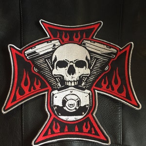 May include: A red and silver embroidered patch with a skull and crossbones design. The skull is surrounded by a stylized engine block with flames on either side. The patch is on a black leather background.