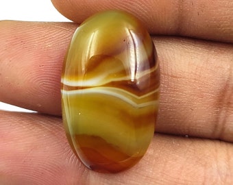 May include: A yellow, brown, and white banded agate cabochon with an oval shape.
