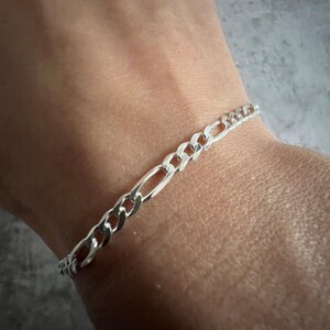 May include: A silver chain bracelet with a curb link design.