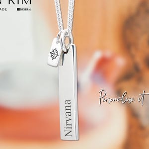 Peut inclure: Un collier en argent avec un pendentif gravé du mot "Nirvana" et un petit charme avec un symbole bouddhiste. Le collier est présenté sur un fond flou avec le texte "Personalised Buddhist Necklace."