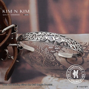 Puede incluir: Un brazalete de brazalete de Om de plata con detalles intrincados. El brazalete está hecho de plata de ley 925 y presenta un delicado símbolo Om.