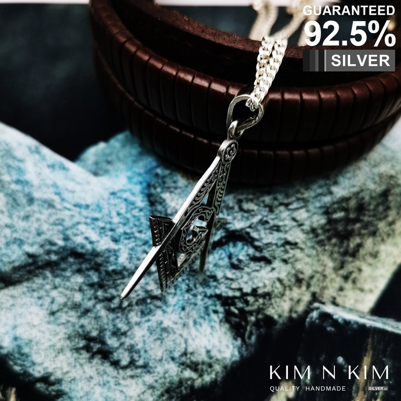 May include: Silver pendant necklace featuring a detailed square and compass design. The pendant is made of 92.5% silver and is guaranteed to be of high quality. The necklace is on a brown leather background.