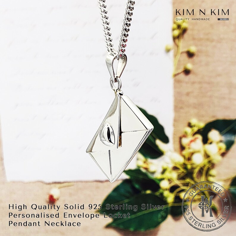 May include: A silver envelope locket pendant necklace on a silver chain. The locket is a detailed representation of a closed envelope with a visible flap. The pendant is hanging against a white and brown background.