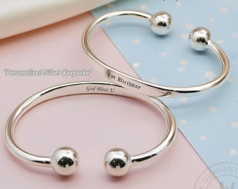 May include: Two polished sterling silver open-ended baby bangles with spherical terminals. One bangle is engraved with the text 1st Birthday and the other with God Bless U. The bracelets are presented as a personalized silver keepsake item.