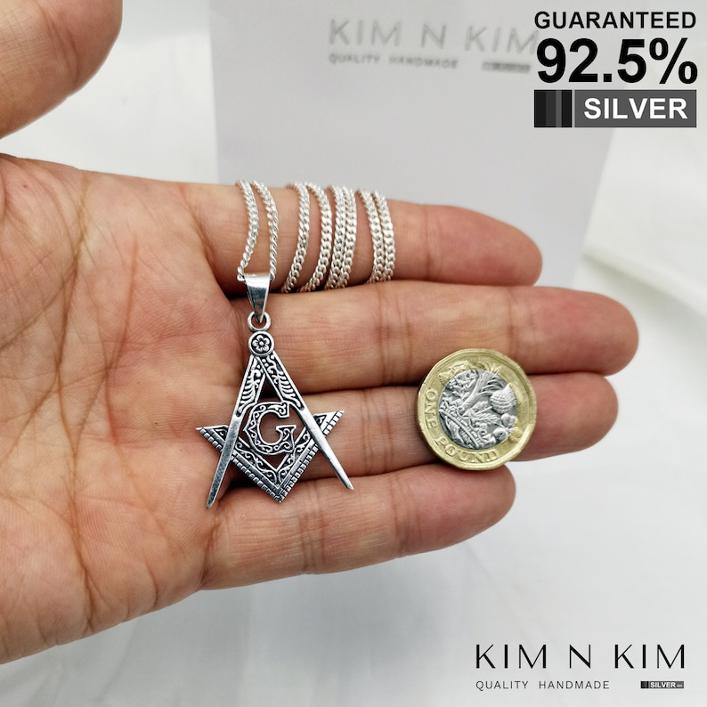 May include: Silver Masonic pendant necklace with a square and compass design and a letter G in the center. The pendant is shown next to a British one pound coin for size comparison. The necklace is guaranteed to be 92.5% silver.